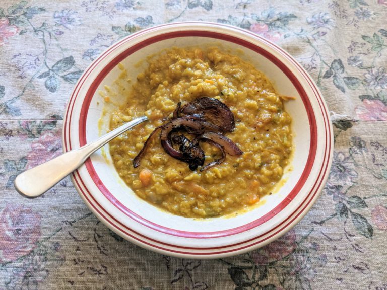 White bowl with a red stripe full of mushy lentil soup with some fried onions as a garnish