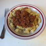 Bowl with red lines on the rim containing twisty (rotini) pasta with tomato sauce on top